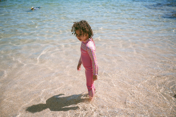 Young child in pink Avaly rashguard playing in shallow beach water on sunny day