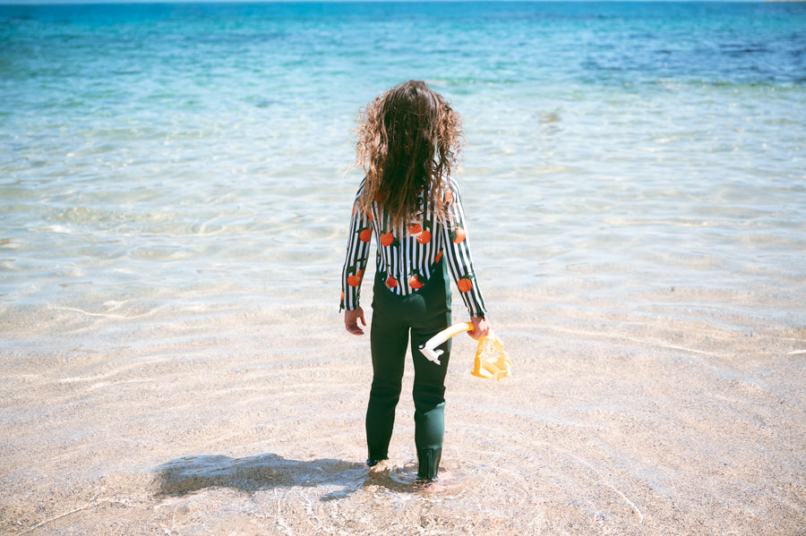 Child in AVALY sustainable swimwear at the beach with ocean behind