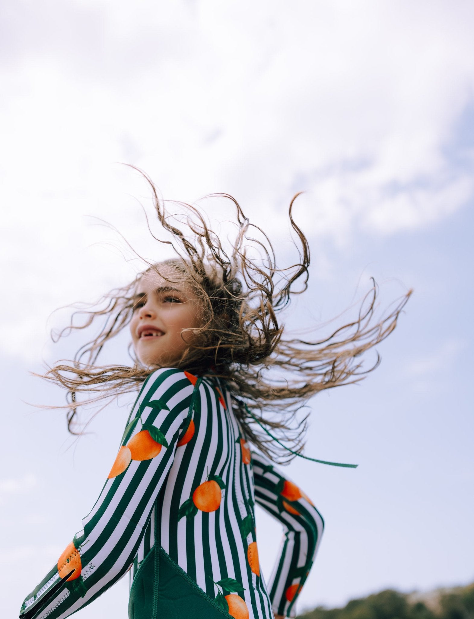 Girl with flowing hair wearing Forest Green & Mandarins wetsuit featuring green stripes and orange citrus print