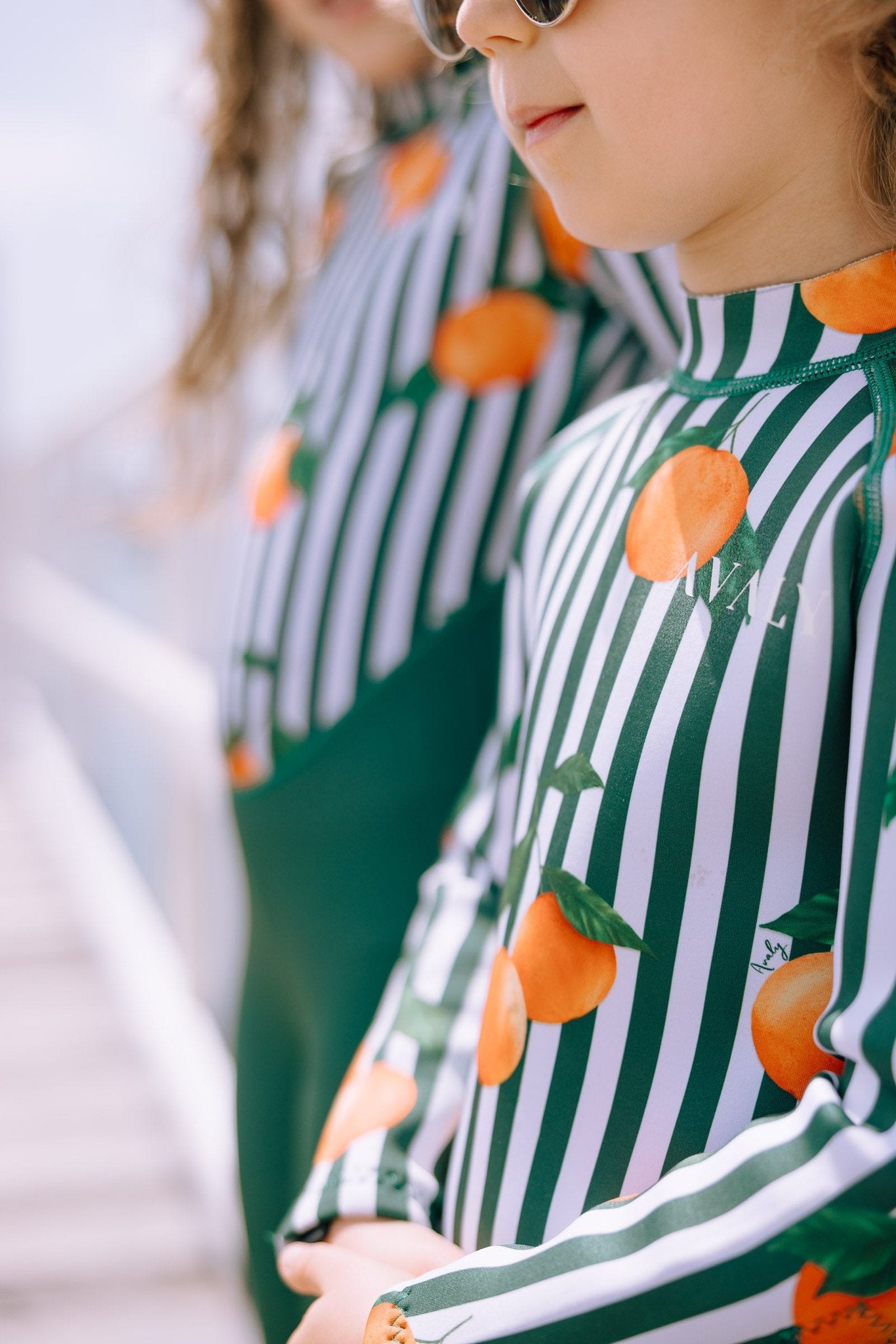 Child wearing Forest Green & Mandarins wetsuit with orange citrus print on green and white striped pattern