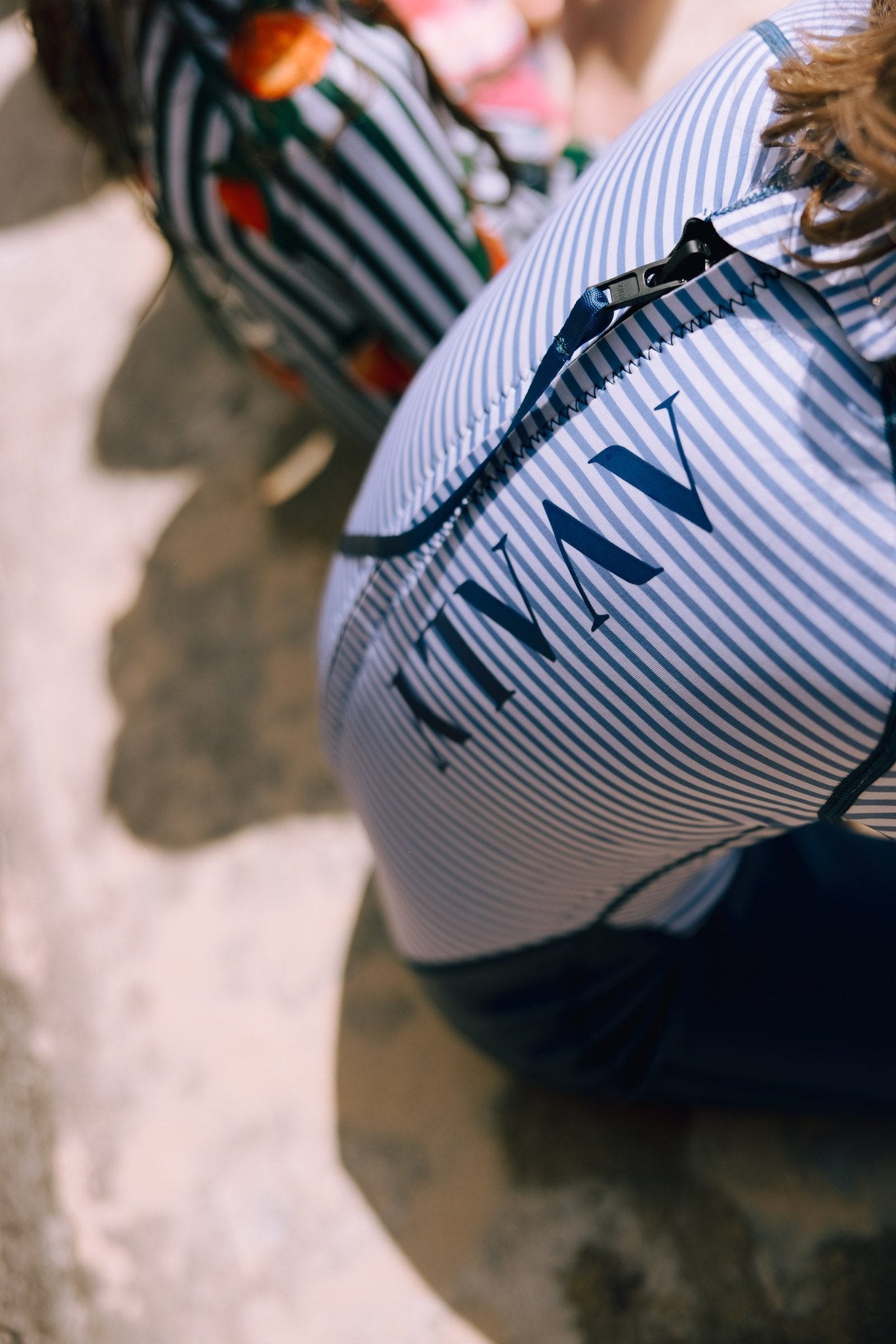 Child wearing Navy & White Striped Kids Sustainable Wetsuit showing close up detail of AVALY logo on striped fabric