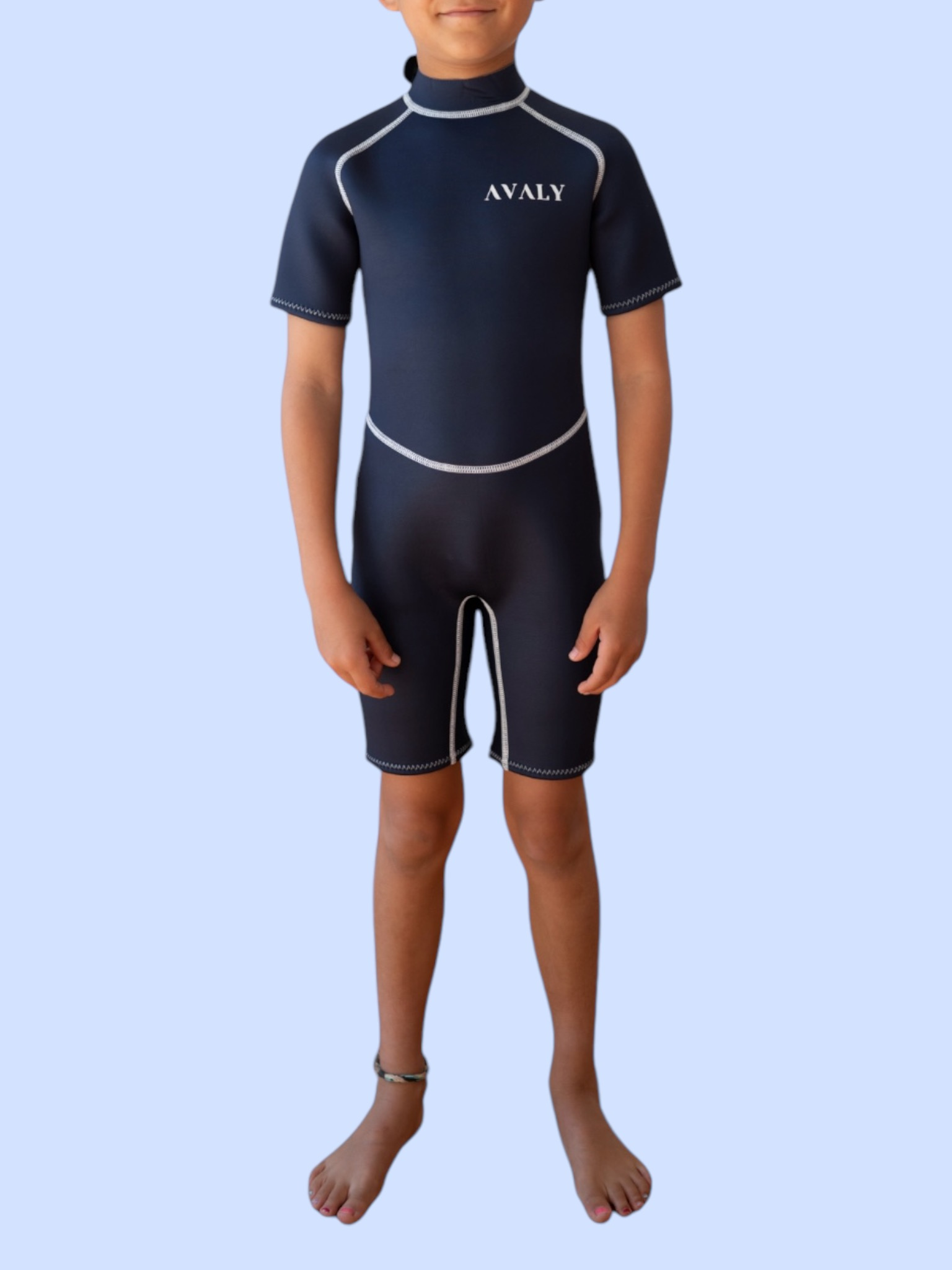 Child model wearing Solid Navy Kids Wetsuit with short sleeves and legs, featuring white contrast stitching and AVALY branding