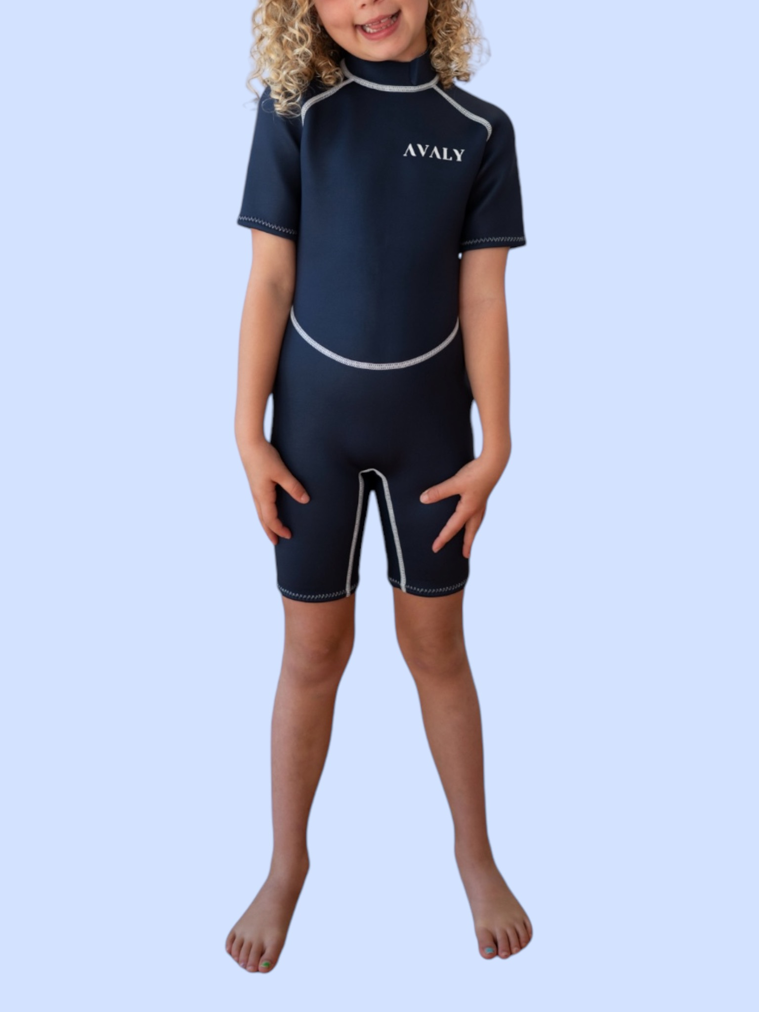 Child model wearing Solid Navy Kids Wetsuit with short sleeves and legs, featuring white contrast stitching and AVALY branding