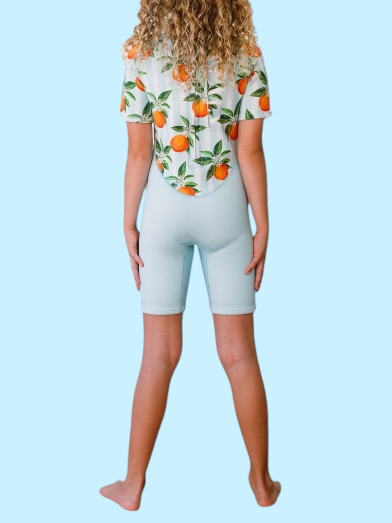 Back view of child wearing Blue Mandarins NOOSA wetsuit showing orange citrus print on white top and blue shorts