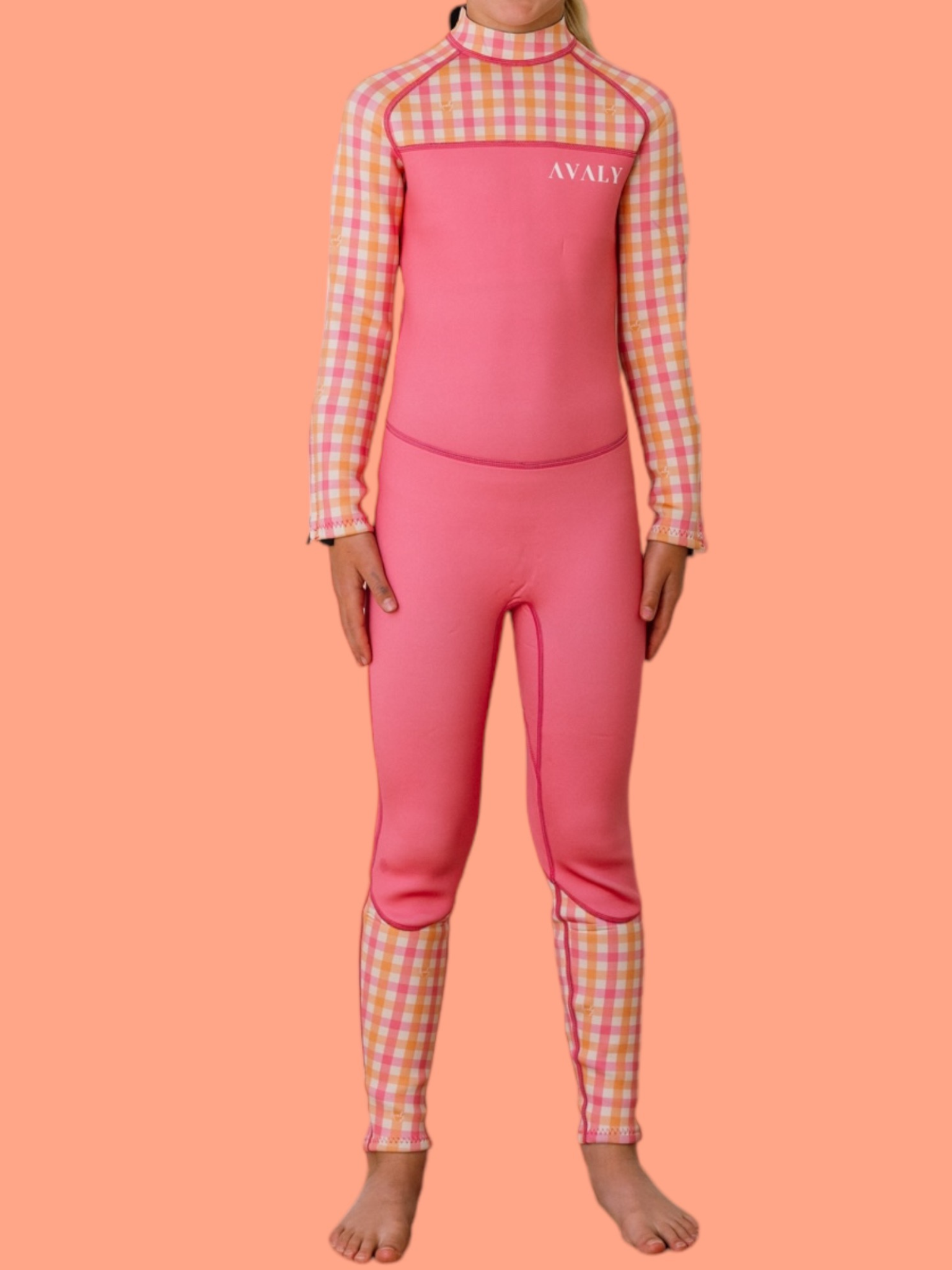 Child model wearing Pink & Orange Gingham wetsuit with checkered sleeves and pink body panel against coral background