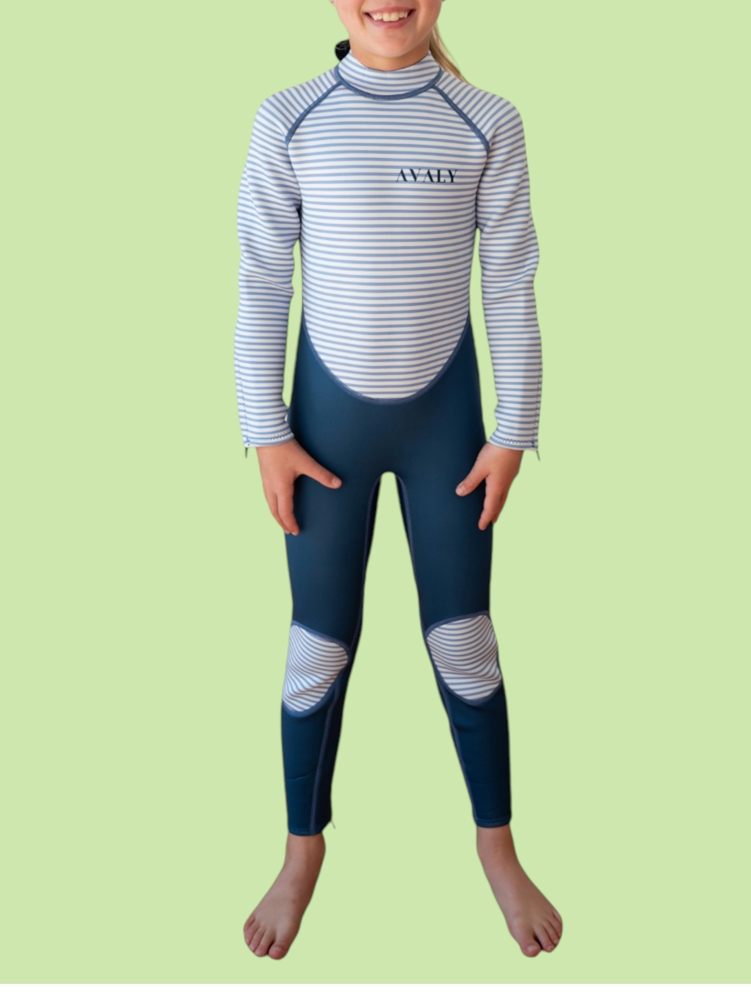 Child model wearing Navy & White Striped Kids Sustainable Wetsuit with blue and white horizontal stripes on green background