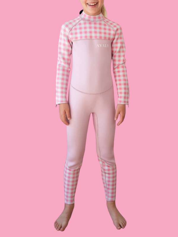 Child model wearing Pink Gingham Kids Sustainable Wetsuit with pink and white checkered sleeves and leg panels