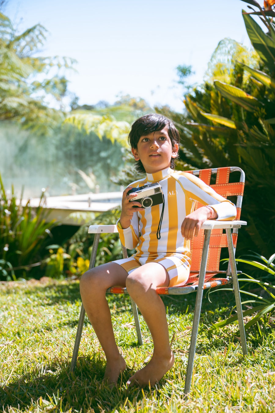 Boy in an AVALY yellow stripe springsuit holding a vintage camera by the pool