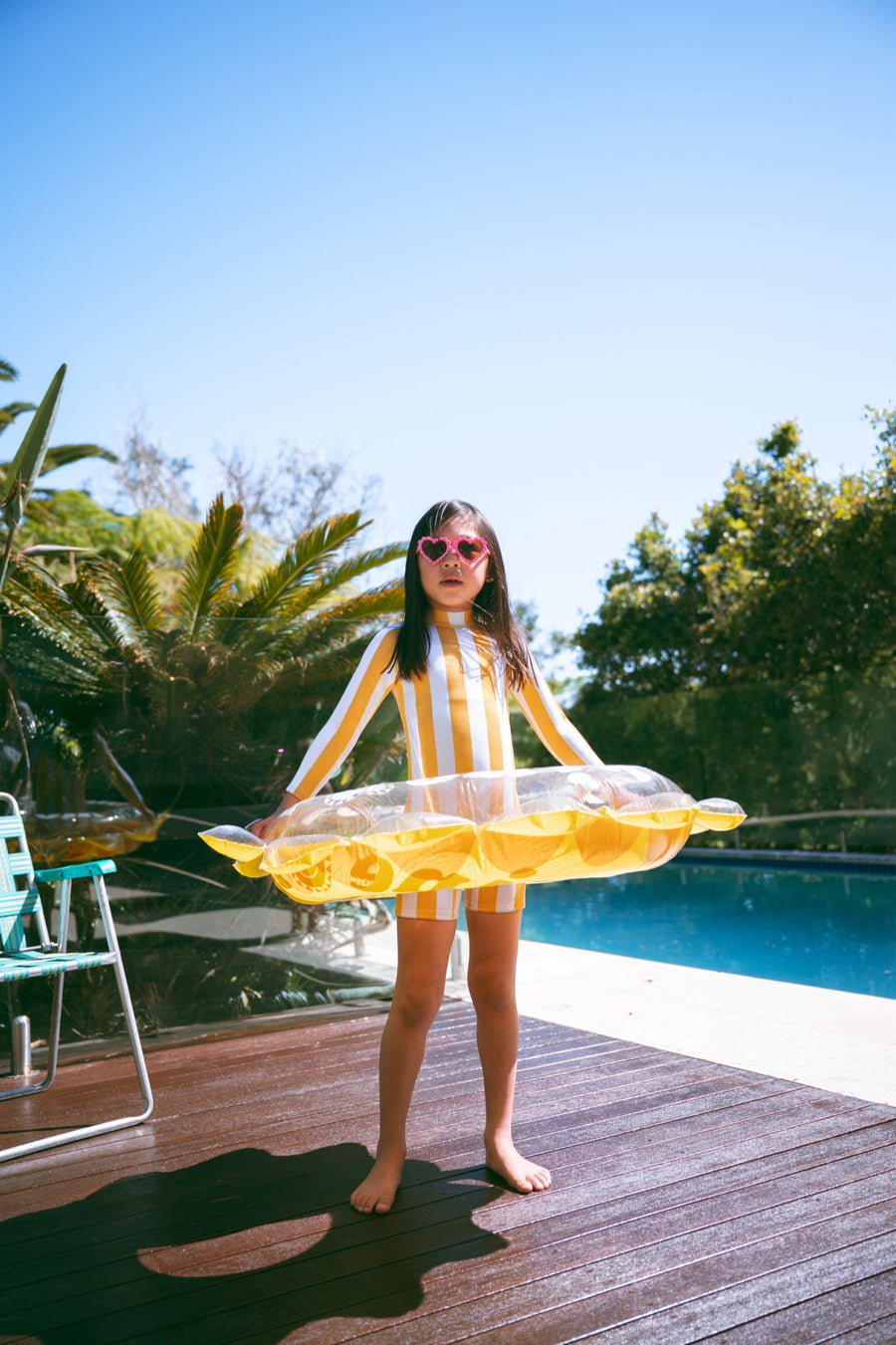 Girl in an AVALY yellow stripe springsuit with heart sunglasses by the pool