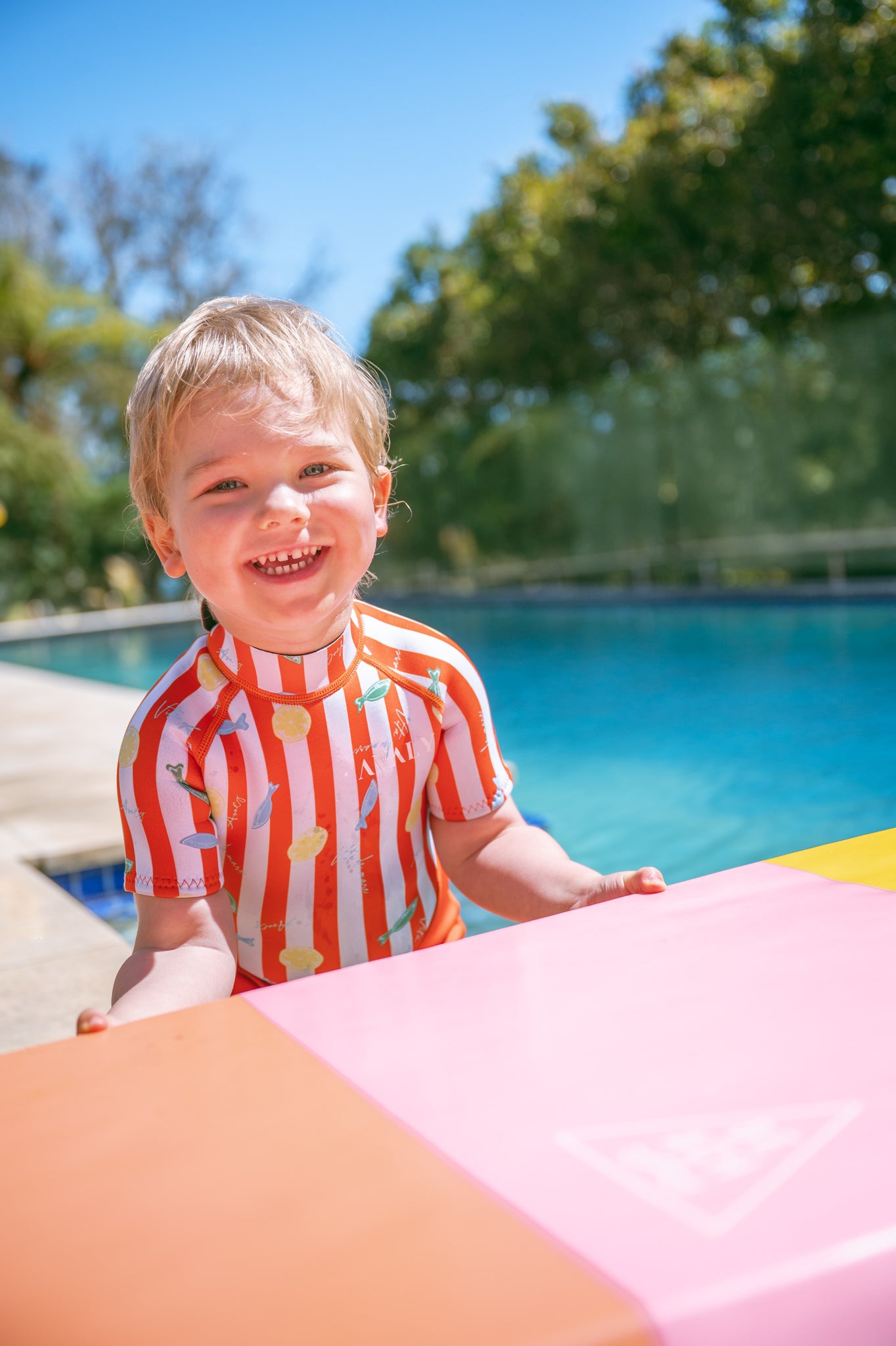 Happy toddler in AVALY swimwear by the pool on a sunny day