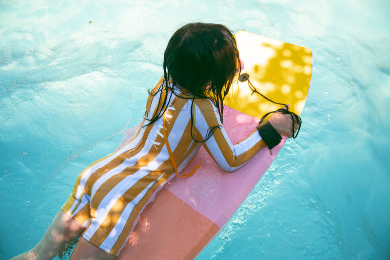 Child on boogie board in turquoise water wearing AVALY wetsuit