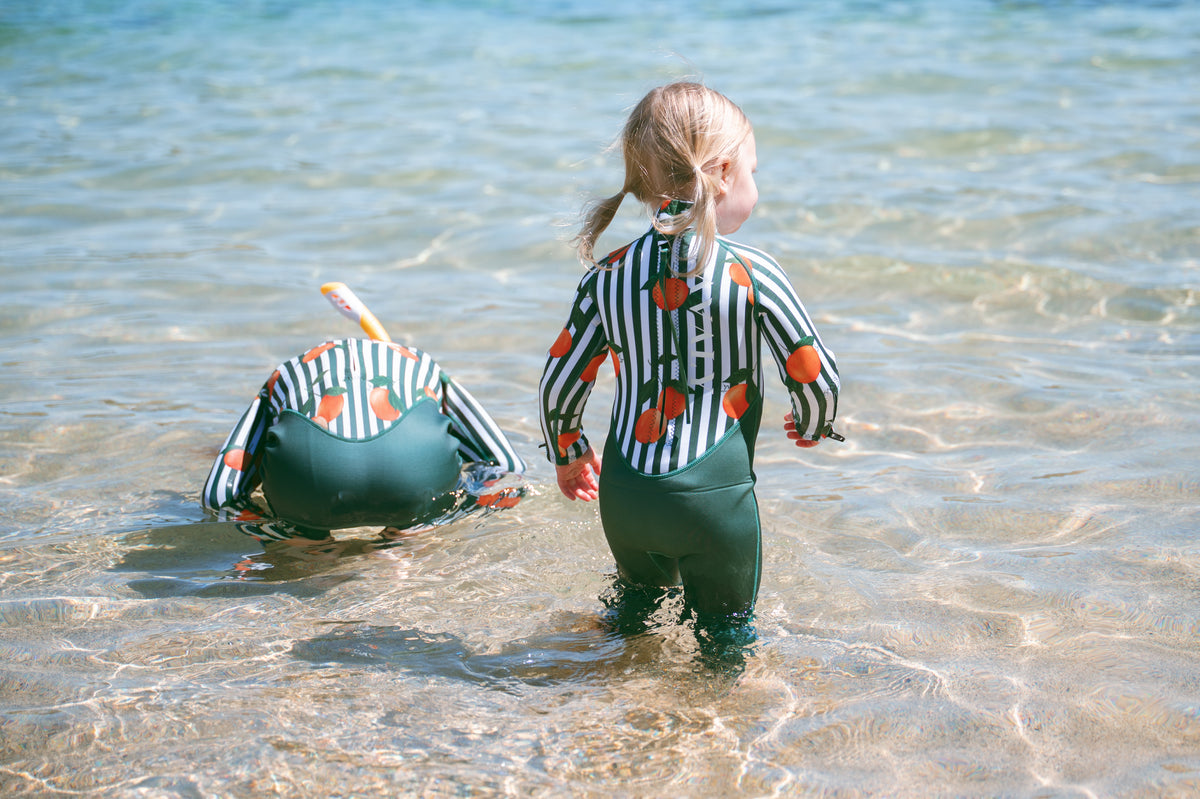 Two children playing together in crystal clear ocean water wearing AVALY wetsuits