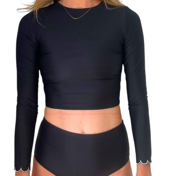 Woman wearing black long-sleeve midi rash top with scalloped cuff detail and matching high-waisted bottoms