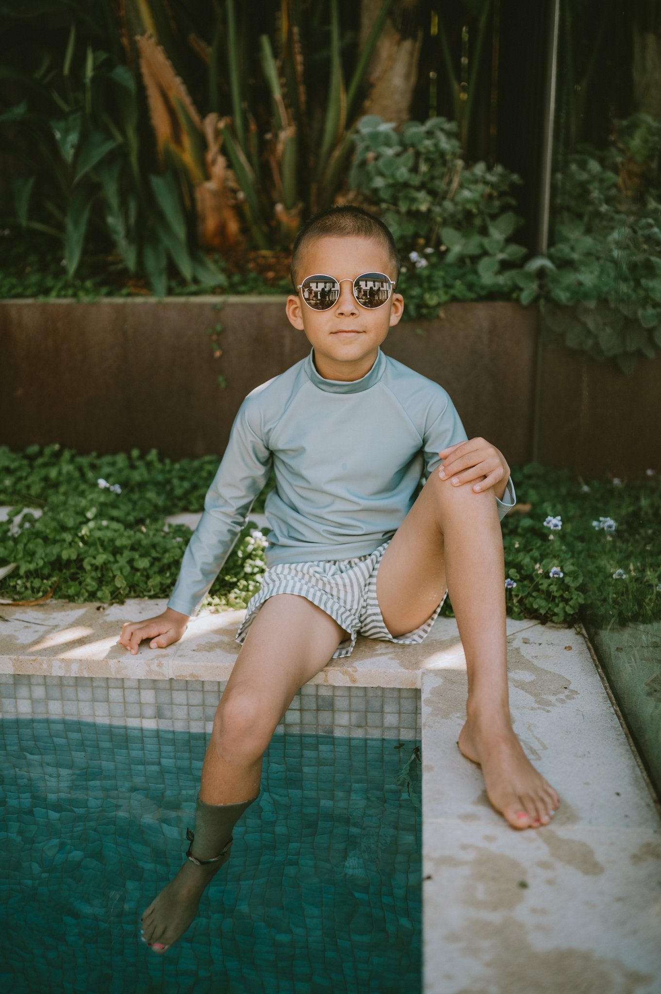 Boy poolside wearing sage long sleeve rashie and Sage striped Vincentia Board Shorts with geometric pattern