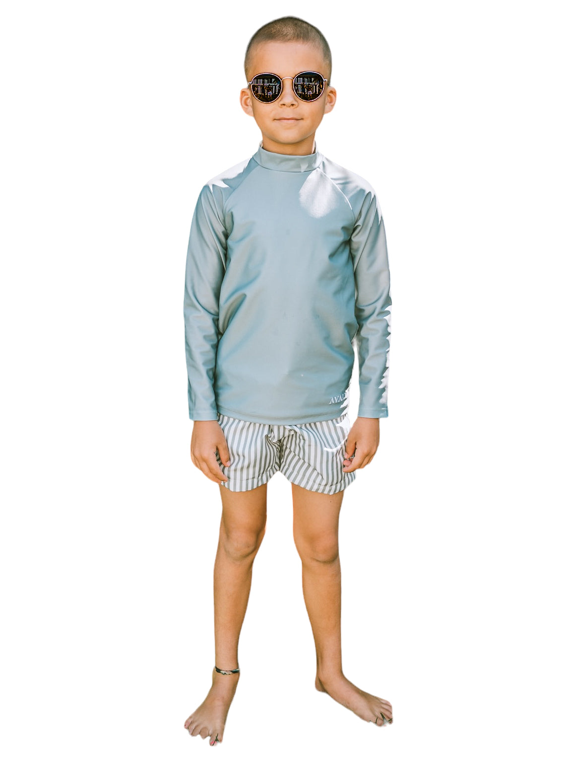 Boy wearing sage green rashie and sage striped Vincentia board shorts with sunglasses on white background