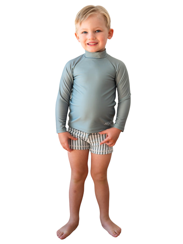 Young boy wearing sage green long sleeve rashie with Sage Striped Moooloolaba sustainable kids trunks featuring gray and white stripes