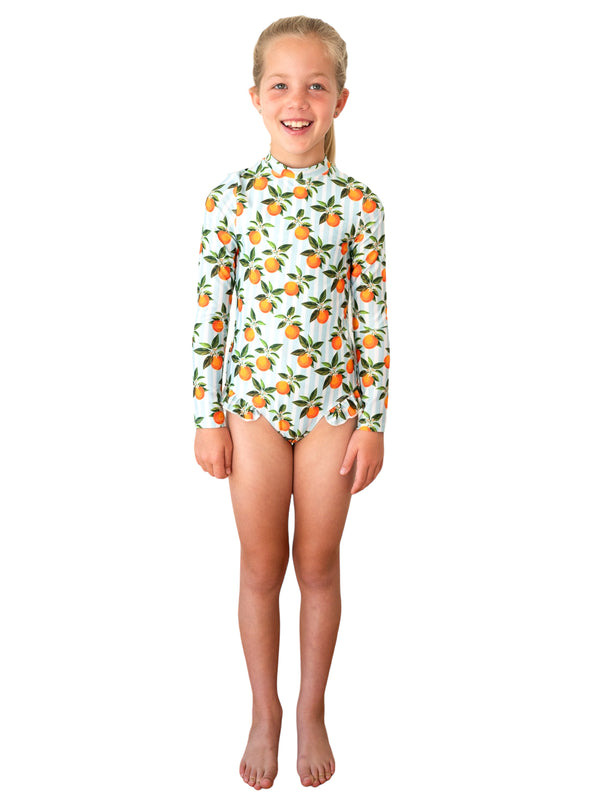 Girl wearing Whitehaven Long Sleeve One Piece with orange citrus fruit print on light blue background
