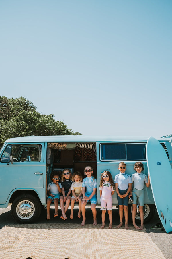 Six children in colorful Avaly swimwear posing by turquoise vintage van on sunny day