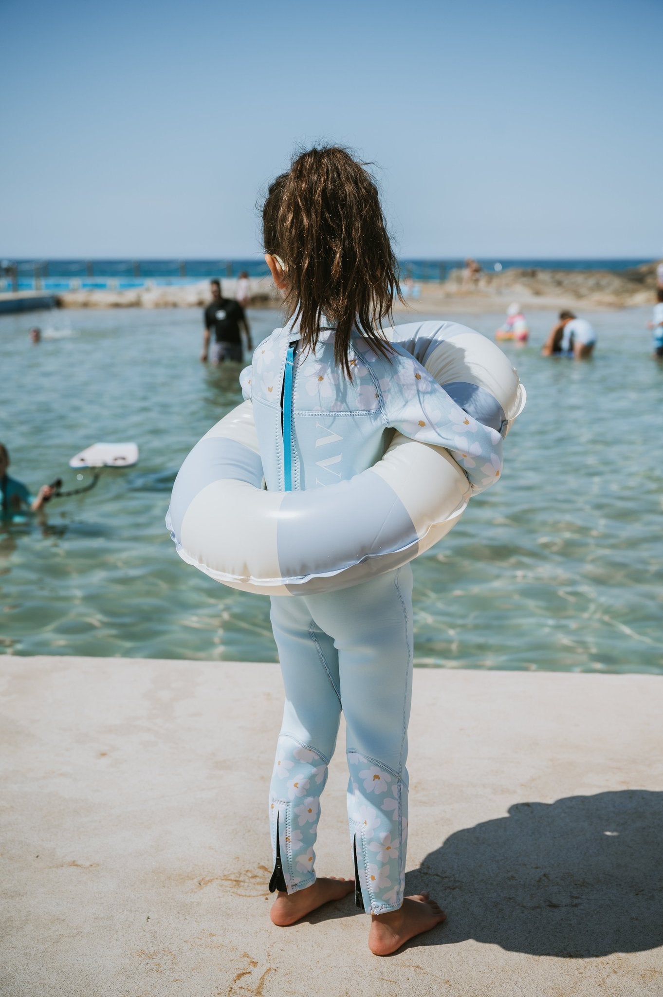 Back view of child in Mint Daisy Kids Sustainable Wetsuit with inflatable ring, showing daisy print and blue zipper detail