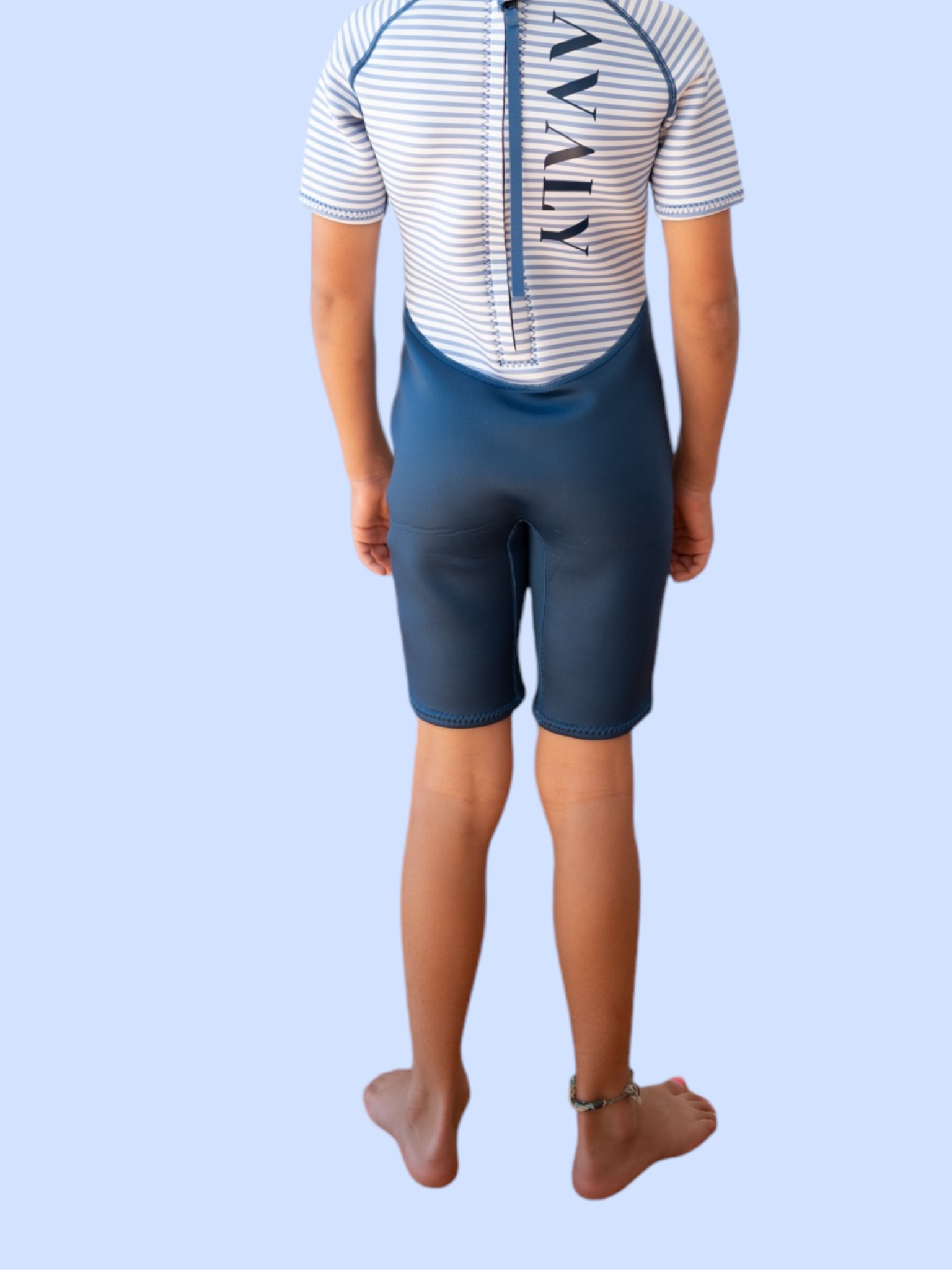 Back view of child wearing Navy Stripe Kids Wetsuit showing white striped pattern and blue shorts with suspenders